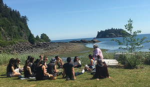 An instructor and a group of students sitting near a rocky shore in Haida Gwaii